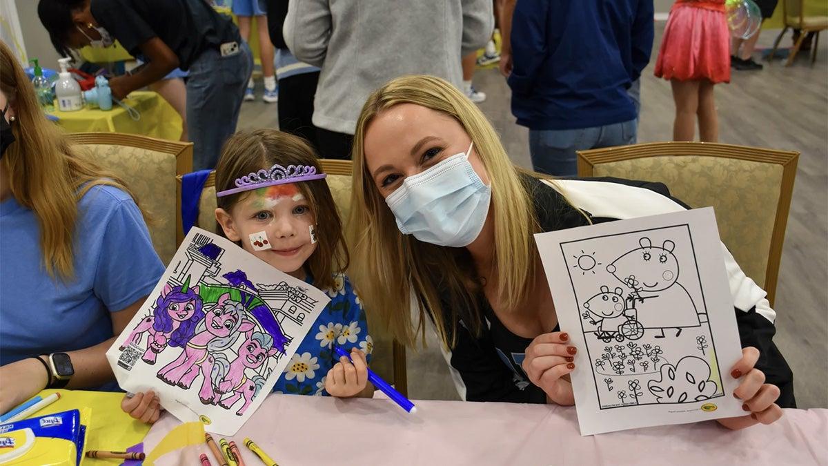 UNC-Chapel Hill student holding up drawing with young child also holding up their drawing.